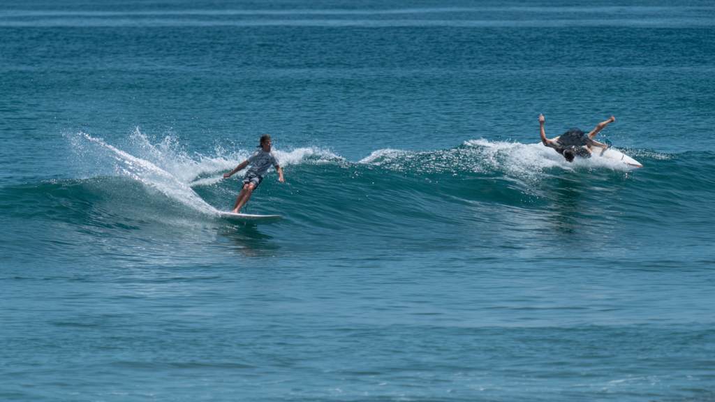 Surfer demonstrating proper back paddling technique swinging wide behind another rider in crystal blue water