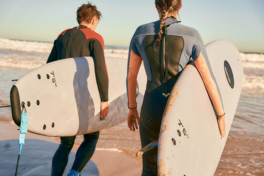 Back view of surfers with surfboards in wetsuit entering towards ocean for surfing on waves